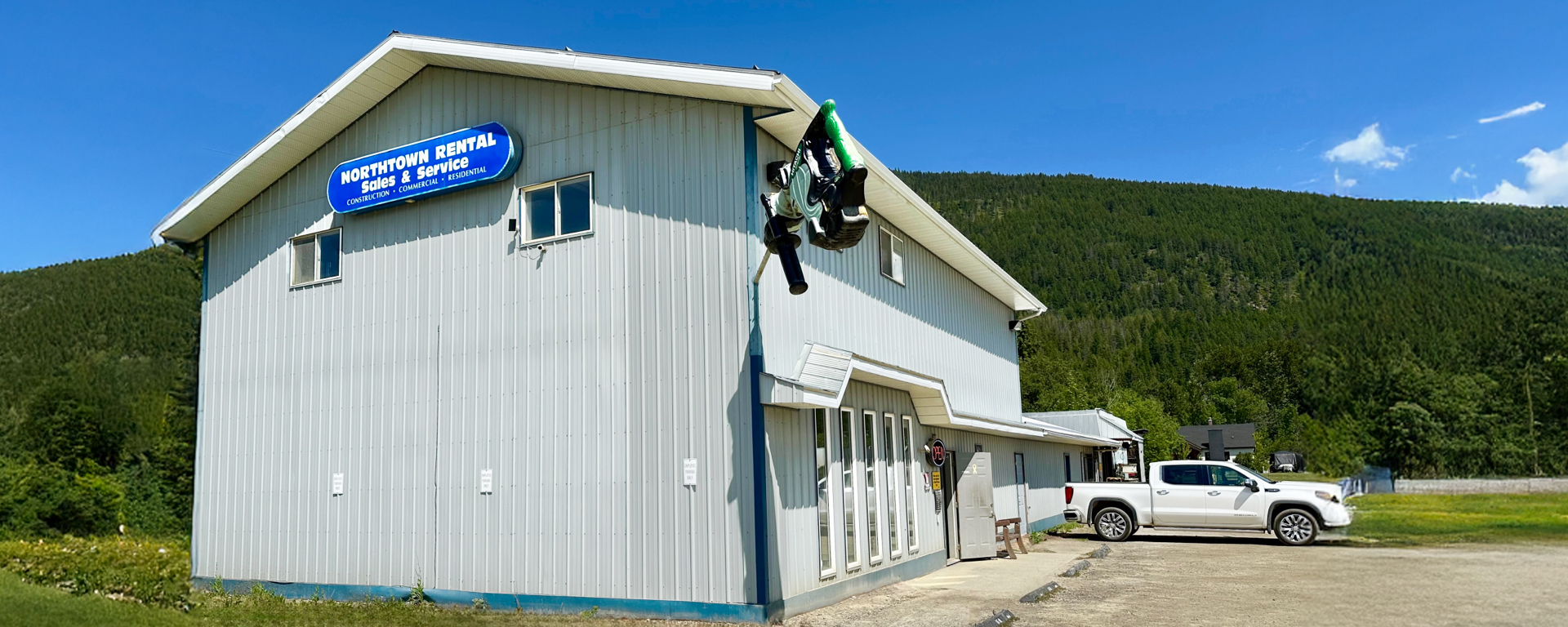 Exterior of the white and blue Northtown Rental building, with forested mountains and blue skies in the background