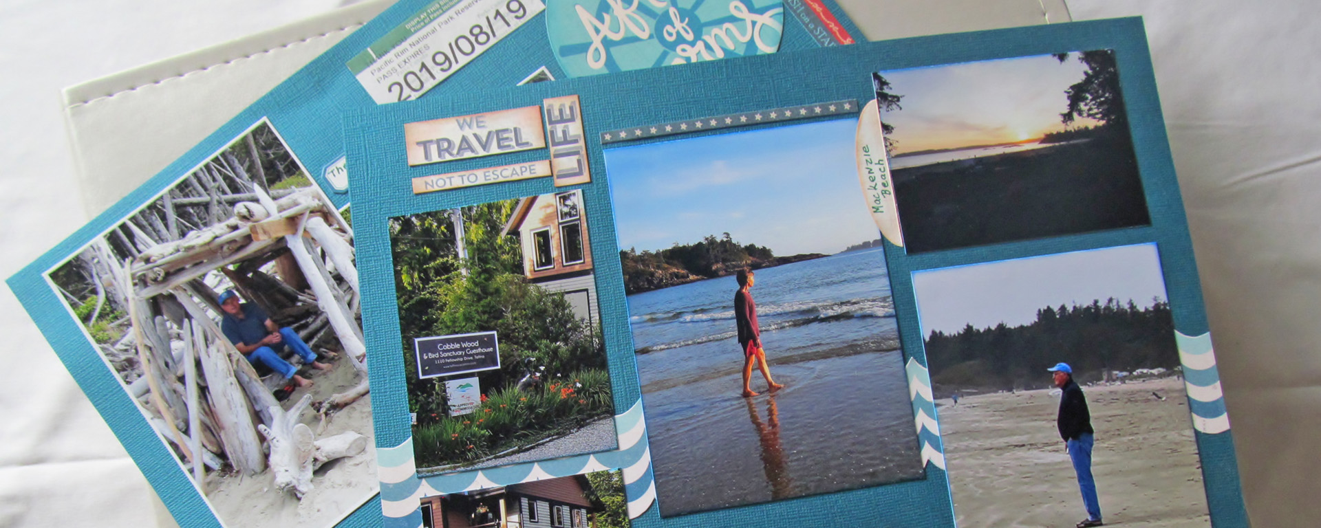A picture of scrapbook pages done in blue tones. There’s several photos on the pages, showing people walking along a beach and visiting a town, plus decorative word text. 