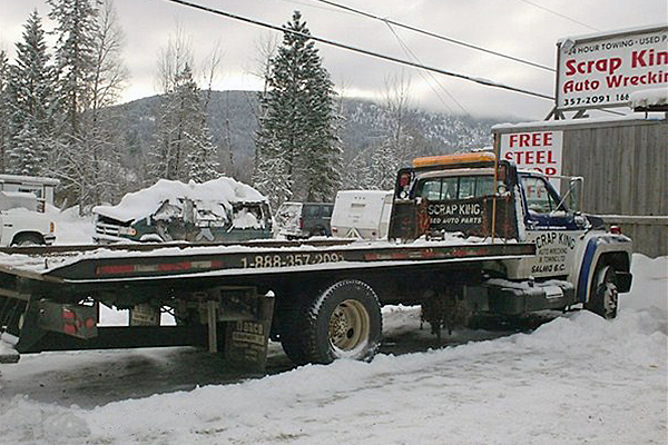 flat deck trailer and truck parked in the snow advertising Scrap King Auto Wrecking and Towing.