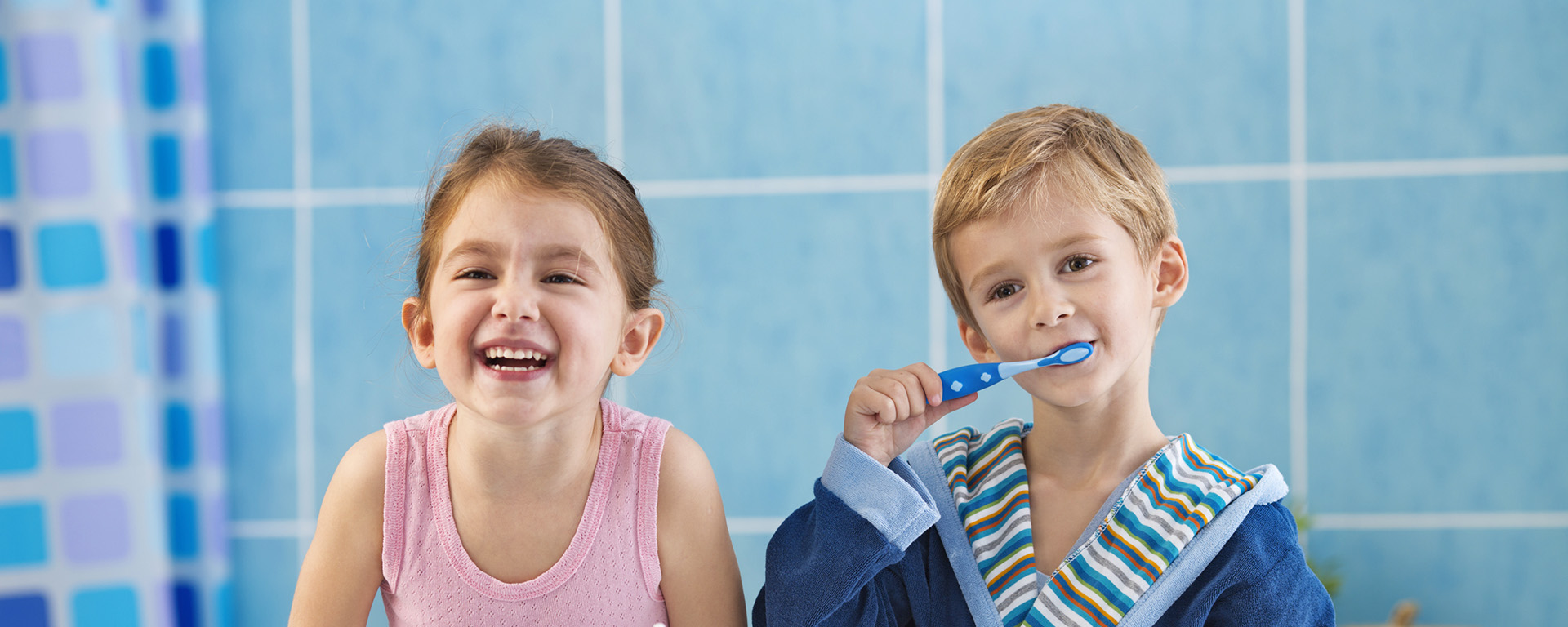 a little boy in a robe standing brushing his teet standing next to a little girl in a pink tank top in a bathroom 