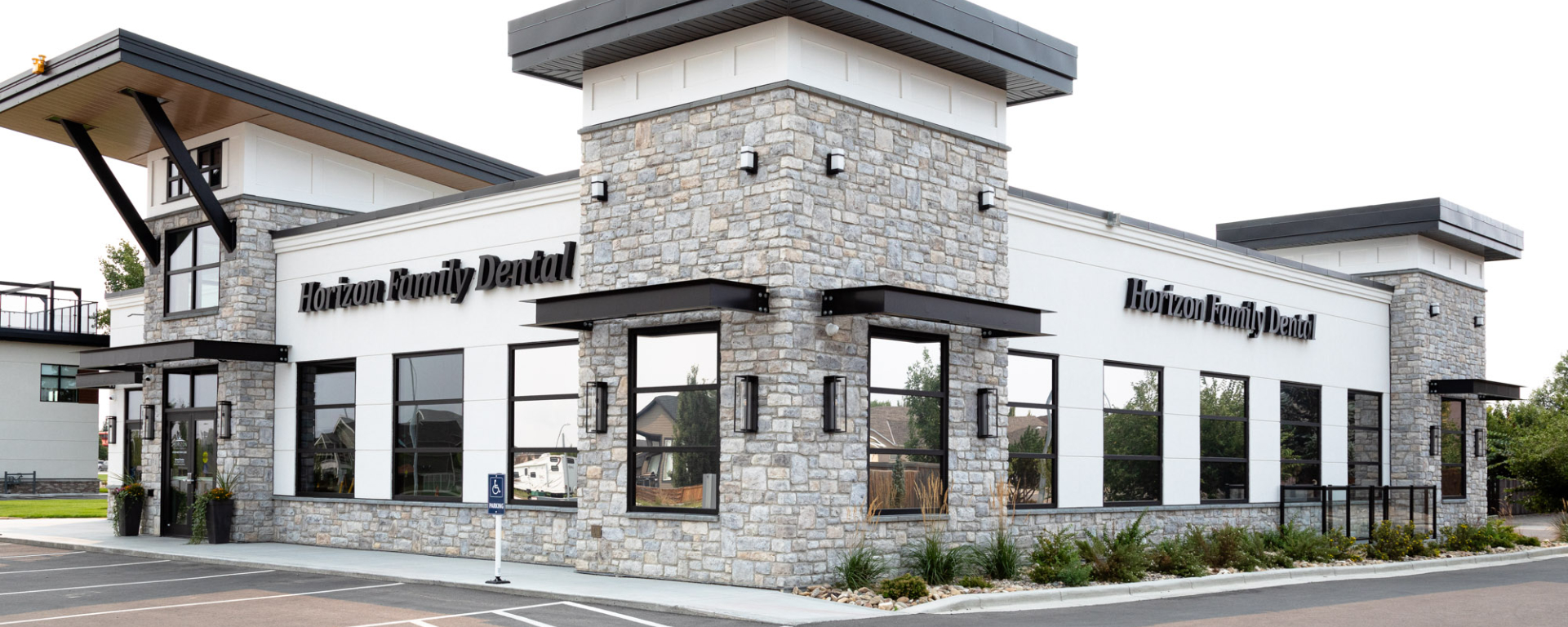 Modern Horizon Family Dental building with white siding, stone masonry, and black-framed windows under a bright sky. 
