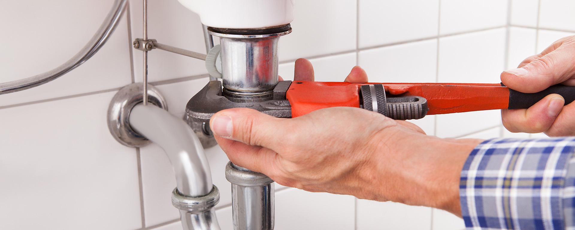 Plumber holding pipe wrench unscrewing a drain pipe. 