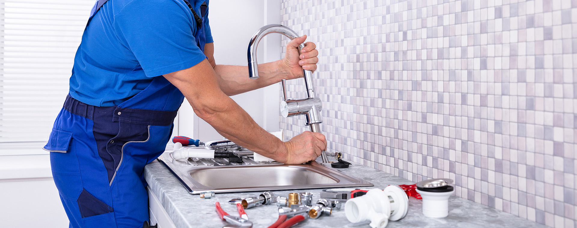 A plumber installs a new faucet in a modern kitchen. 