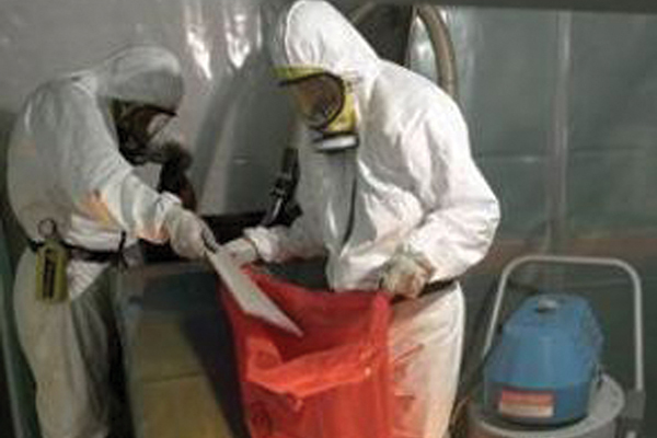 Two men in white gear putting drywall pieces in a red bag
