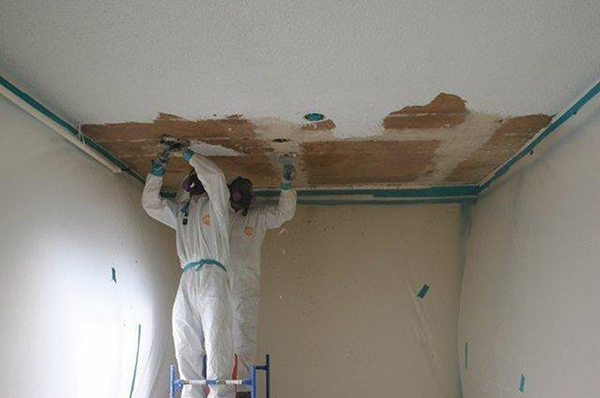 Two men in white gear scraping a ceiling