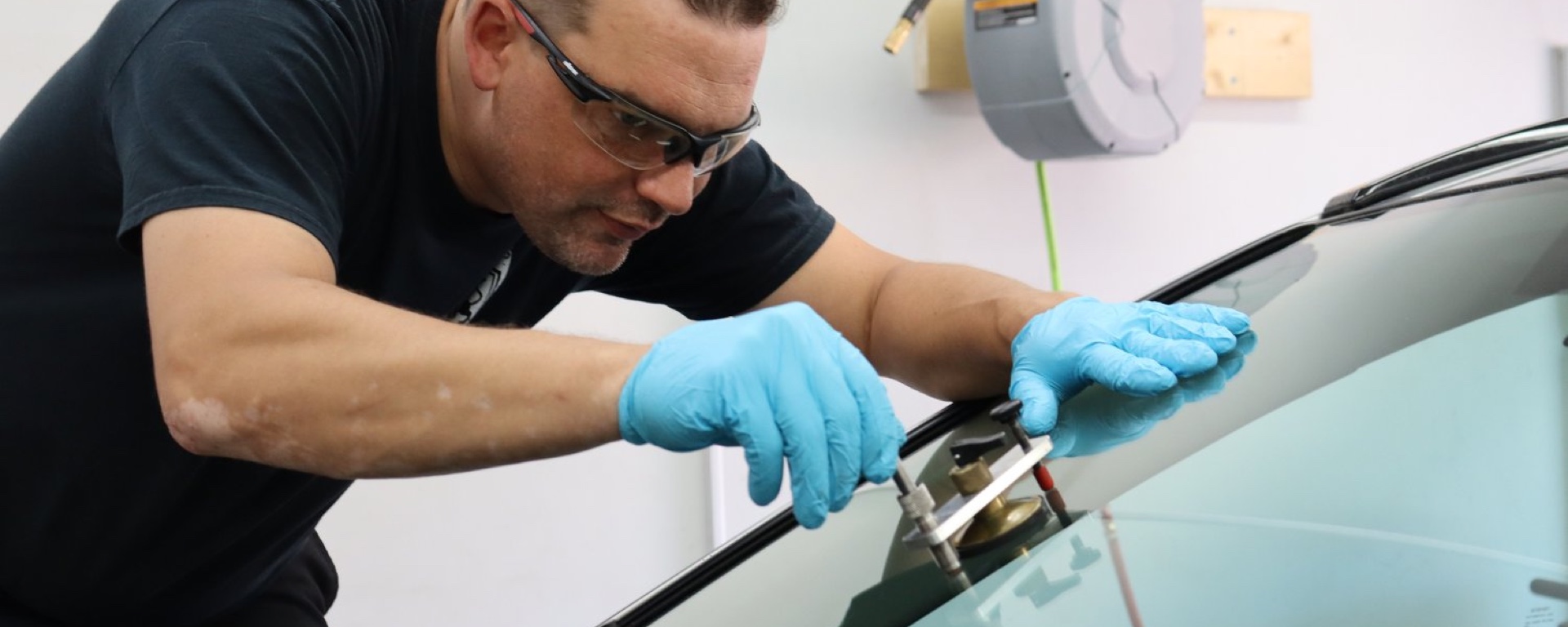 Close-up of a man wearing blue nitrile gloves fixing glass on a windshield 