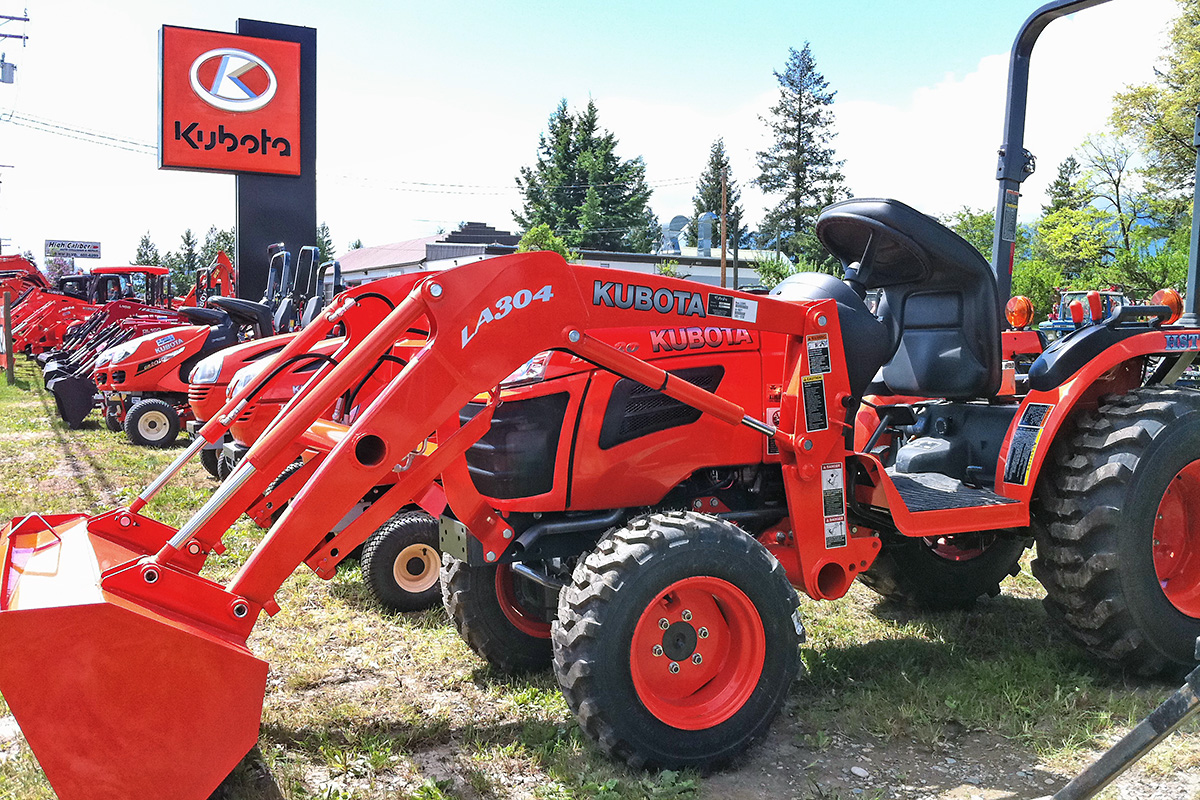 Red tractors parked outside by an exterior sign advertising Kubota 