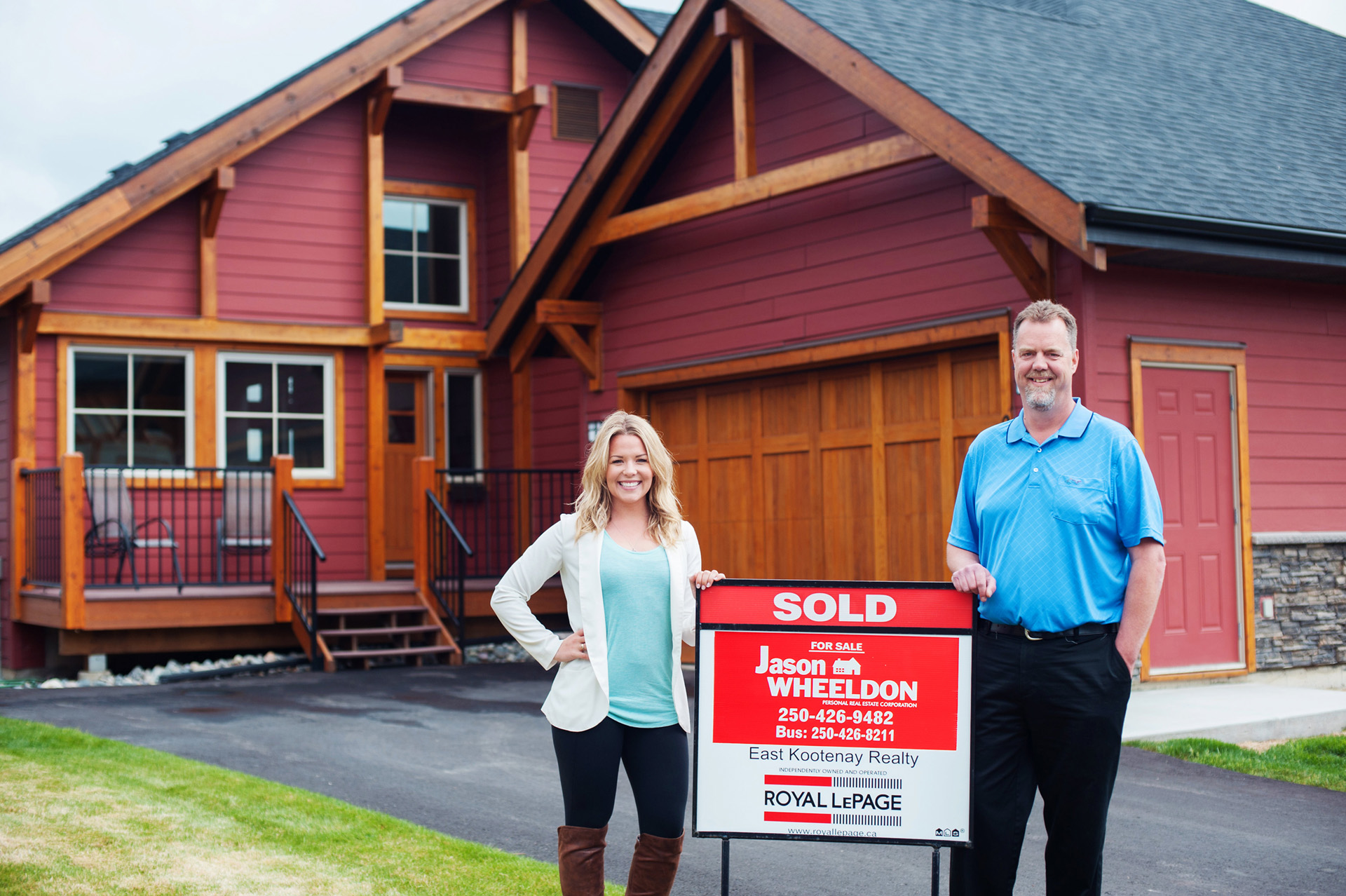 Kaytee Wheaton and Jason Wheeldon standing in front of a home next to a sold sign, 