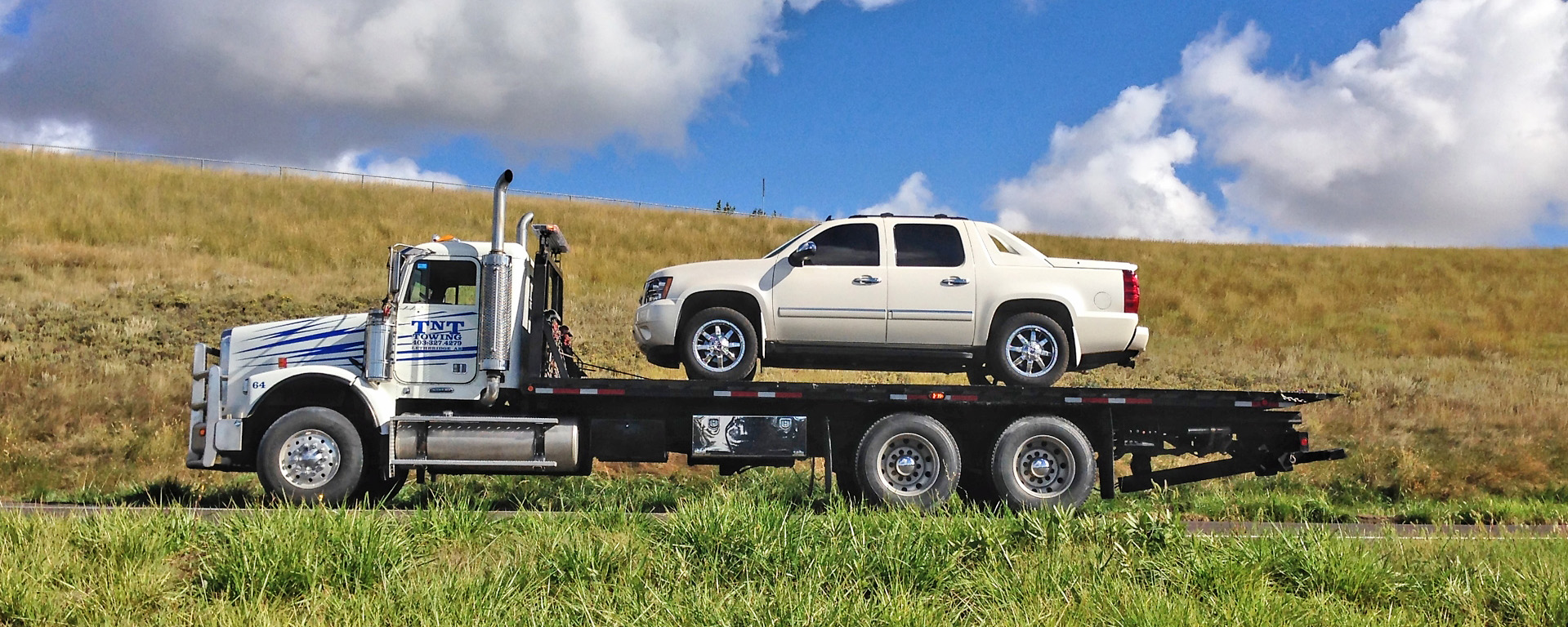 Semi tow truck hauling a white truck on the flat deck advertising T N T Towing 