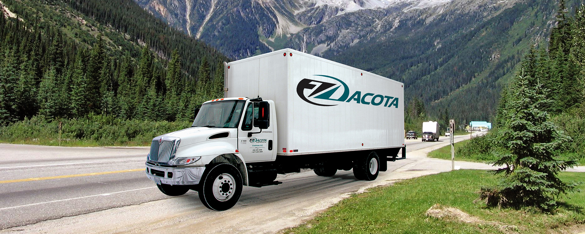 A large Dacota cube van is shown on a scenic road with mountains in the background. 
