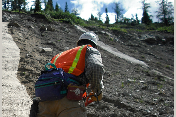 man dressed in safety gear measuring a dirt trail