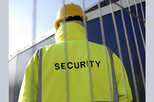 The back of a man standing guard wearing a security jacket