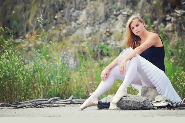 female ballerina sitting down on concrete and a rock 