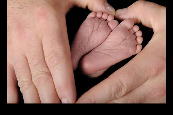adult hands encompassing a newborns feet 