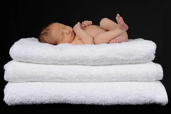 newborn sleeping on white towels folded to make a bed 