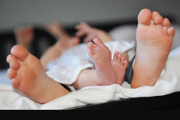 two pairs of bare feet resting at the end of the bed 