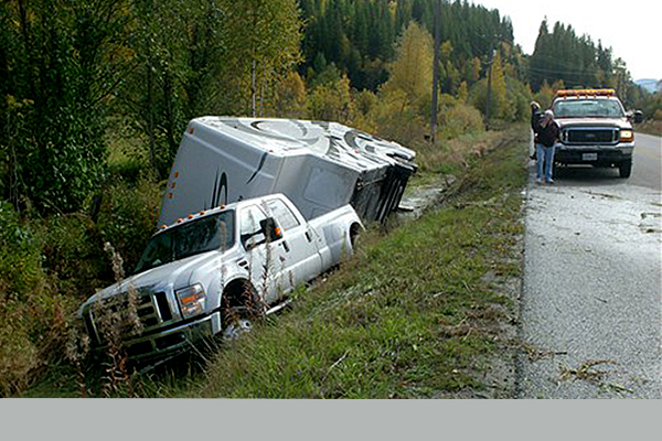 white truck and white camper rolled over in the ditch off the side of the highway