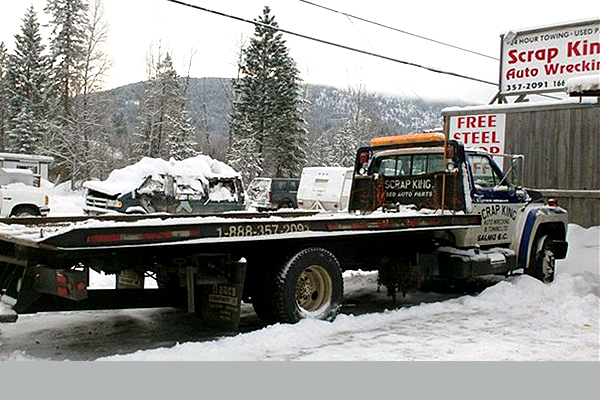 flat deck trailer and truck parked in the snow advertising Scrap King Auto Wrecking and Towing.