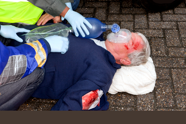 Two paramedics assisting a man laying down with an oxygen mask over his face