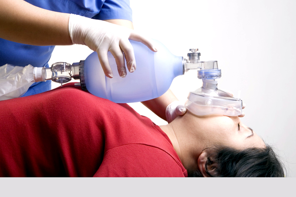 A paramedic using an oxygen pump on a female laying down