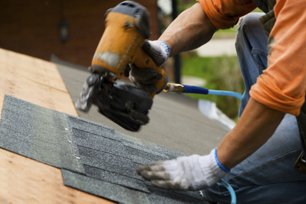 man operating a drill with shingles on a roof
