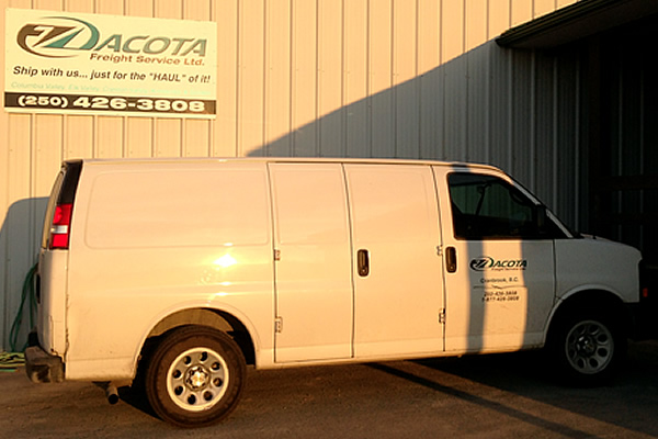white company van advertising Dacota Freight Services parked next to exterior sign advertising Dacota Freight Services