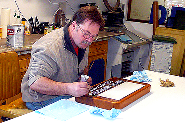 Murray Young sitting at table hand painting a sign 