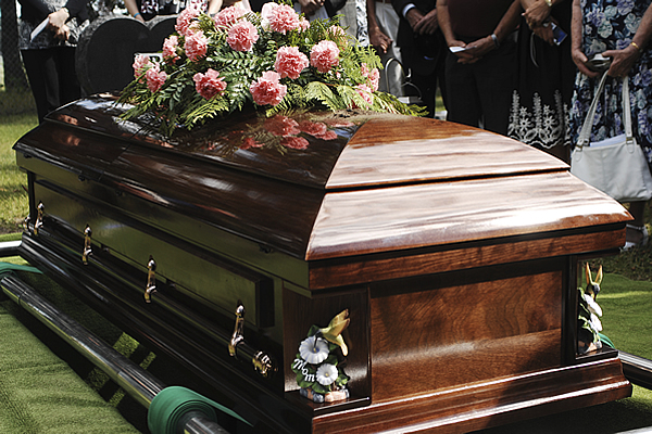 a brown wooden casket outdoors with a pink floral arrangement on top