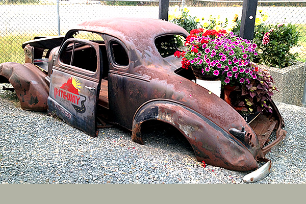 old, abandoned rusted car with flowers and a decal on the door advertising Rite Way RV Services