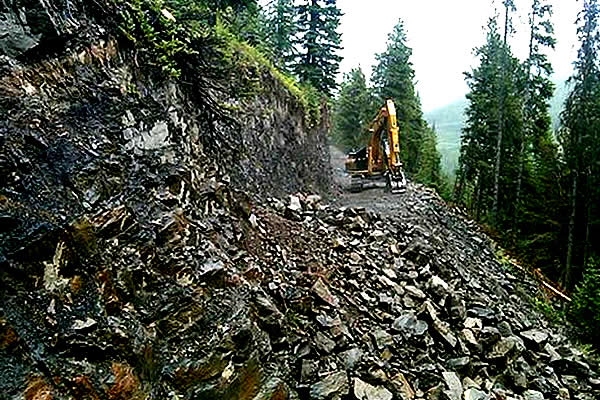a backhoe clearing mounds of rock from a mountain side road 