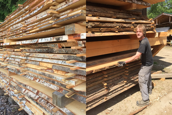 man standing outside next to high piles of horizontally cut wood