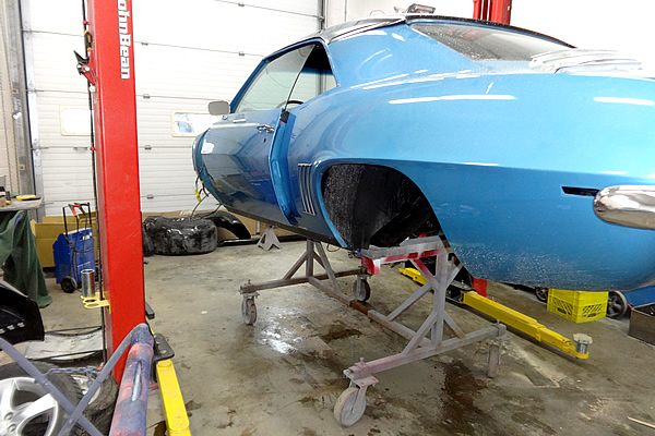 body of a light blue car on a hoist with no engine or tires