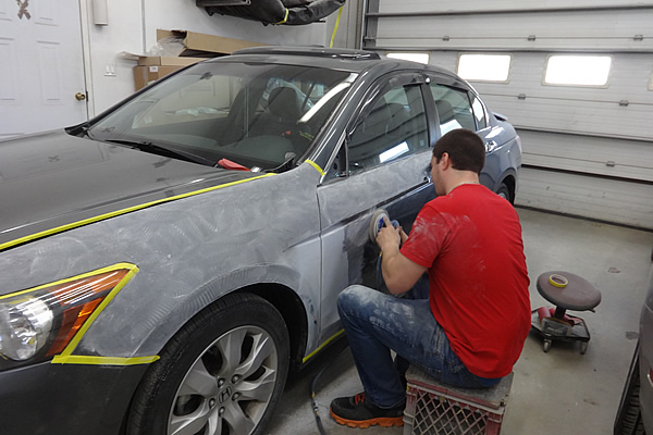 man sitting down detailing the exterior of a gray coloured car door on the driver's side