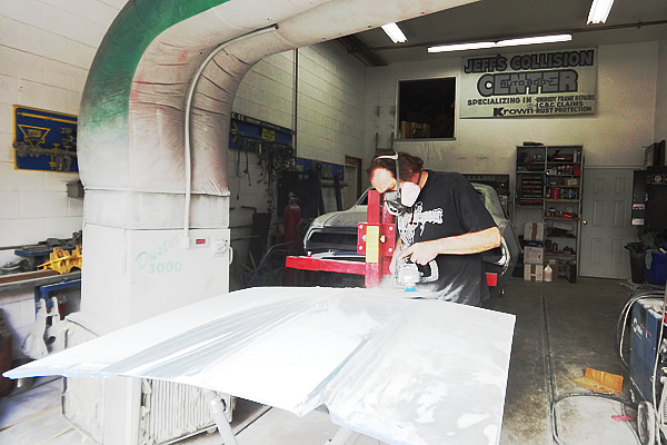 a man wearing proper protective equipment sanding the side of a vehicle on a slabbed table