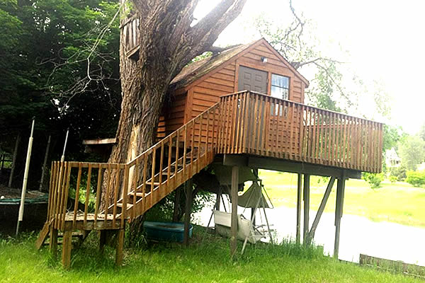 wooden play house built in a tree with wrap around stairs