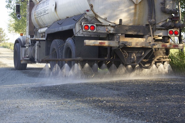 Kan-West truck applying dust control spray to gravel road. 