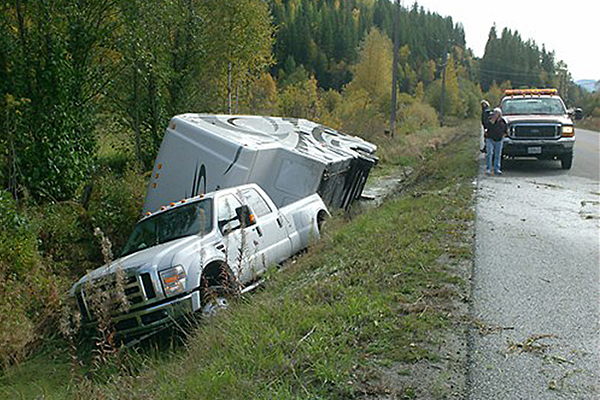 white truck and white camper rolled over in the ditch off the side of the highway