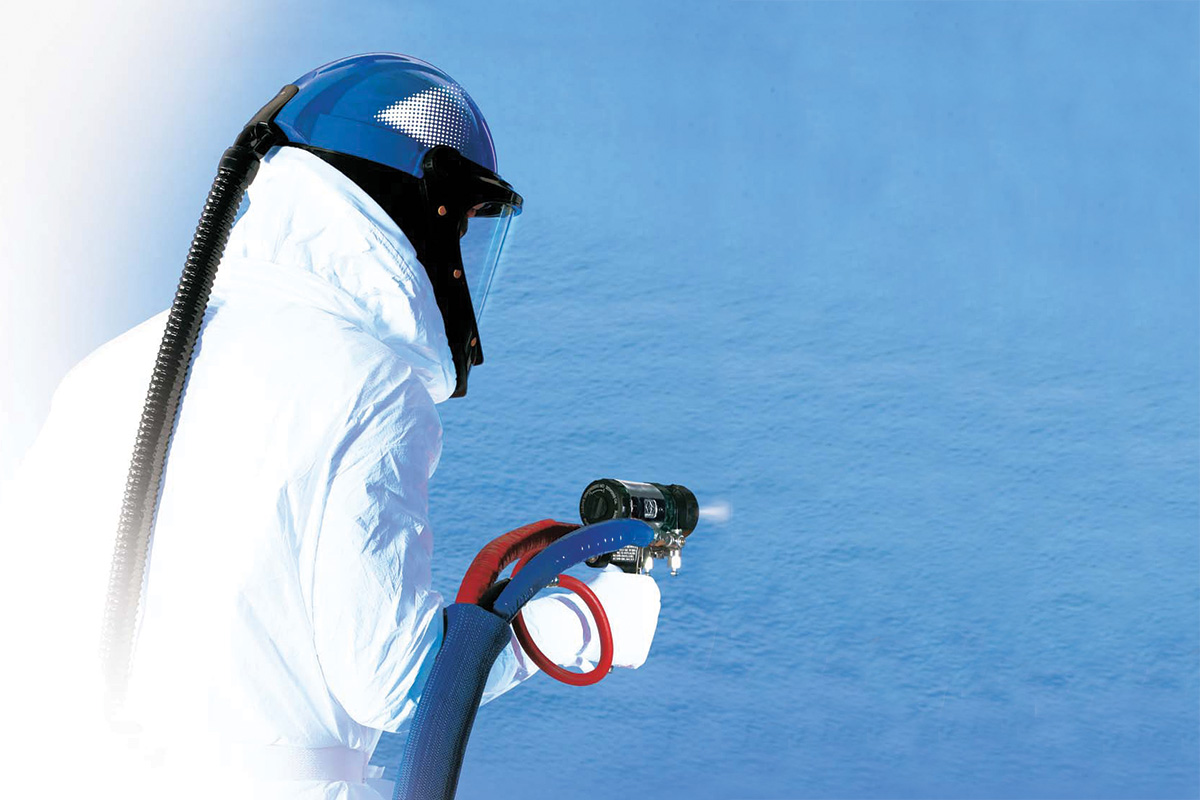 man spraying insulation on a blue coloured wall