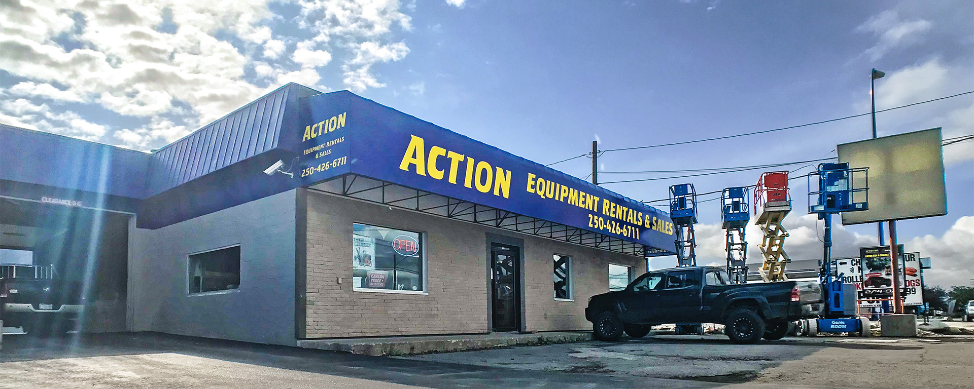 Front entrance of Action Equipment Rental is a grey building with a blue awning and yellow lettering.