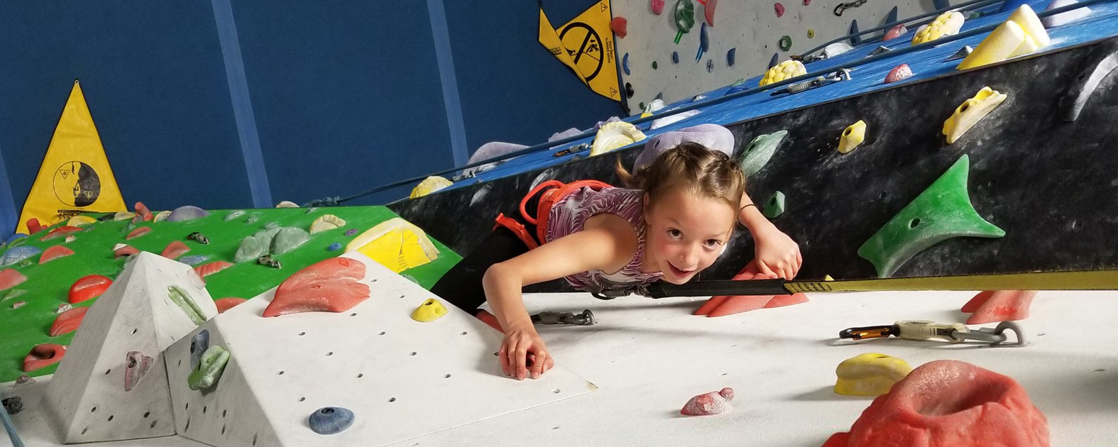 A young girl smiling while climbing up a wall at Arq Mountain Centre in Cranbrook 