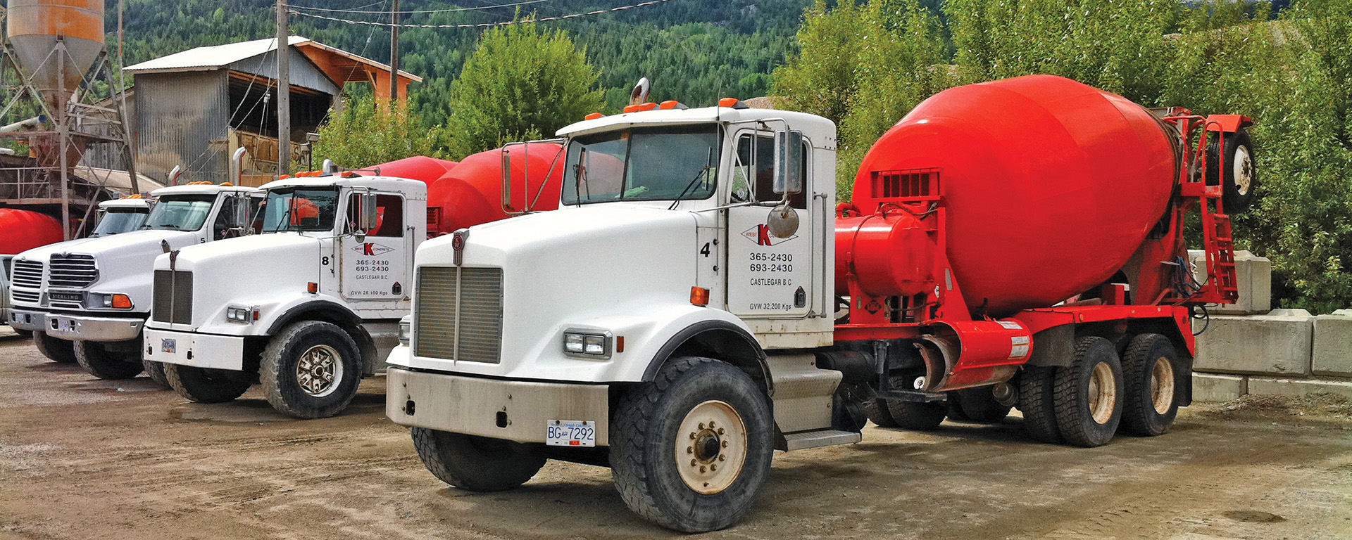 white semi trucks hauling a red concrete mixing tank 