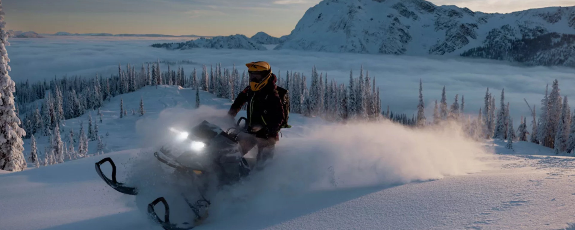 Snowmobiler riding through the powder with mountains in the background 