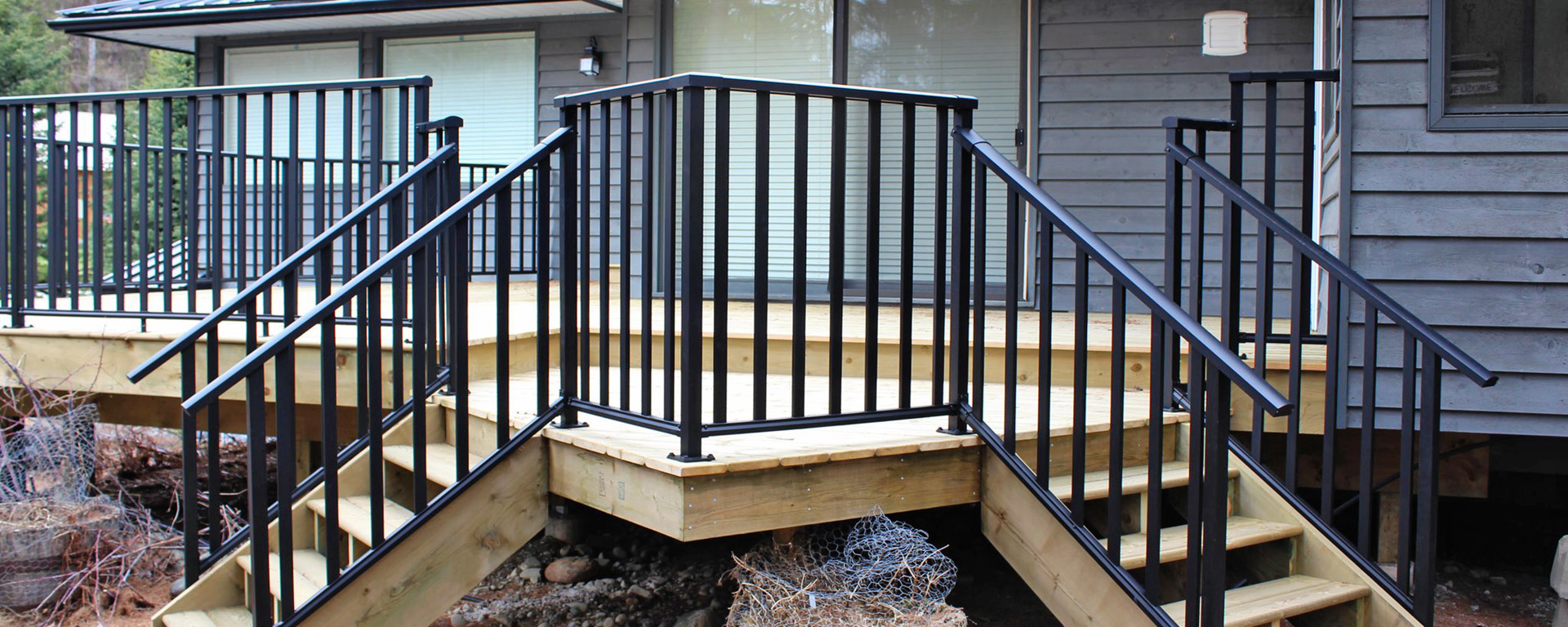 A newly built wooden deck with two separate sets of stairs. The deck is finished with a black metal railing. 